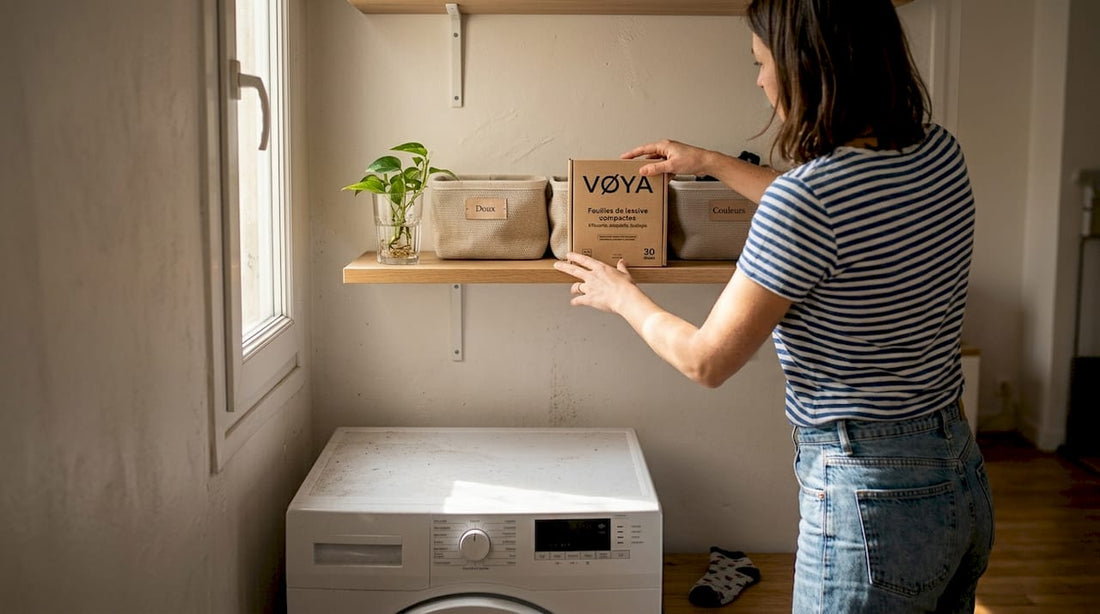 Une femme range soigneusement des feuilles de lessive compactes dans un petit coin buanderie, optimisant l’espace de rangement avec ingéniosité.